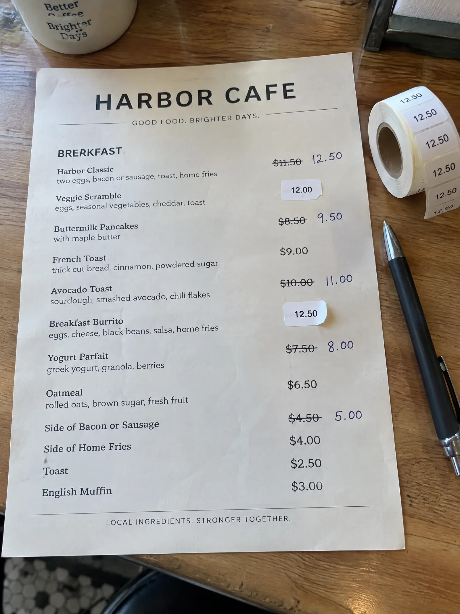 Et printet Harbor Cafe-menukort dækket af overstregede priser og prisklistermærker ved siden af en kuglepen og en rulle mærkater.